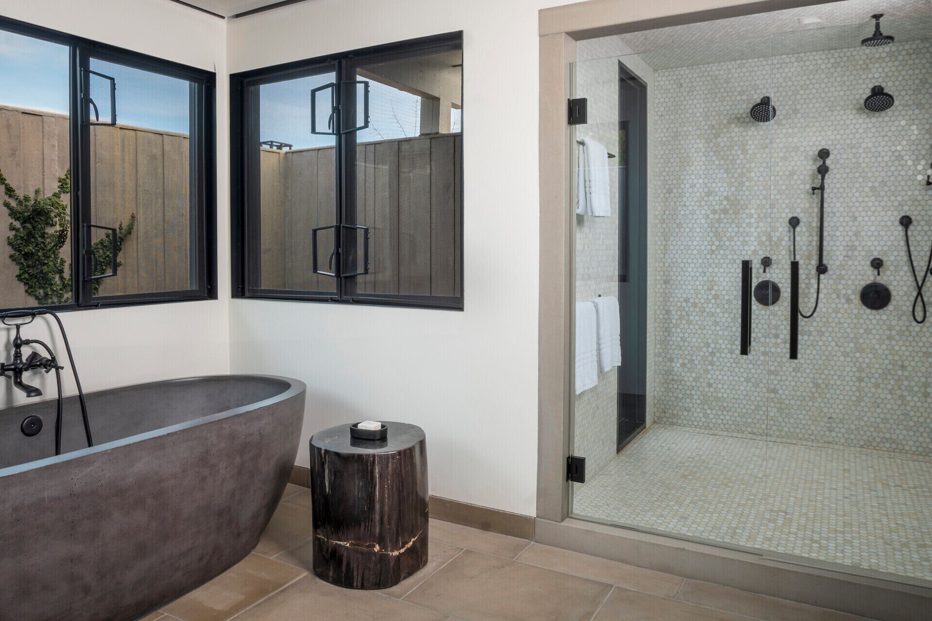 A modern bathroom with a freestanding bathtub, a glass-enclosed shower area, and a large window with a view of the outside.