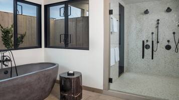 A modern bathroom with a freestanding bathtub, a glass-enclosed shower area, and a large window with a view of the outside.
