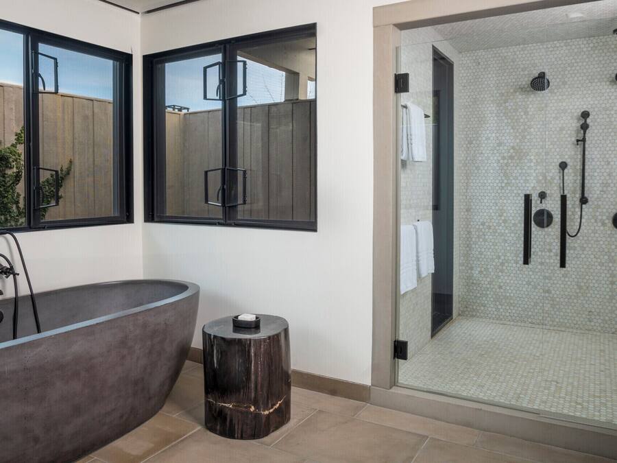 A modern bathroom with a freestanding bathtub, a glass-enclosed shower area, and a large window with a view of the outside.