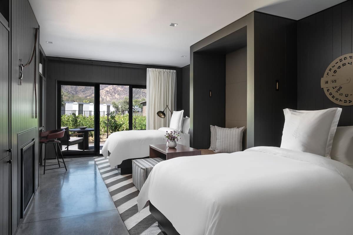 Ein modernes Hotelzimmer mit zwei Betten, einem Essbereich mit Tisch und Stühlen sowie Blick ins Freie.