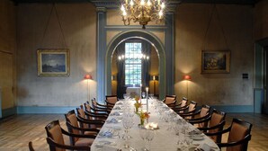 A long dining table set for a formal meal with chairs on both sides, chandeliers, and framed artwork on the walls. - Kasteel de Wittenburg (Wassenaar)