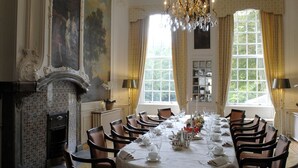 A formal dining room with a long table set for a meal, flanked by chairs, a chandelier, and large windows with curtains. - Kasteel de Wittenburg (Wassenaar)