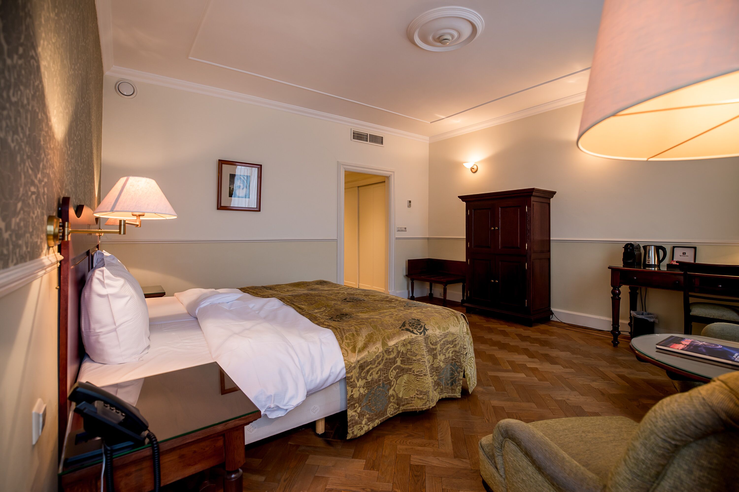 A hotel room with a bed, a desk, a chair, a lamp, a cabinet, and a door.