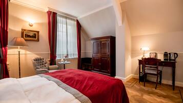 A hotel room with a large bed, a desk with a lamp, a chair, a cabinet, and a window with curtains.