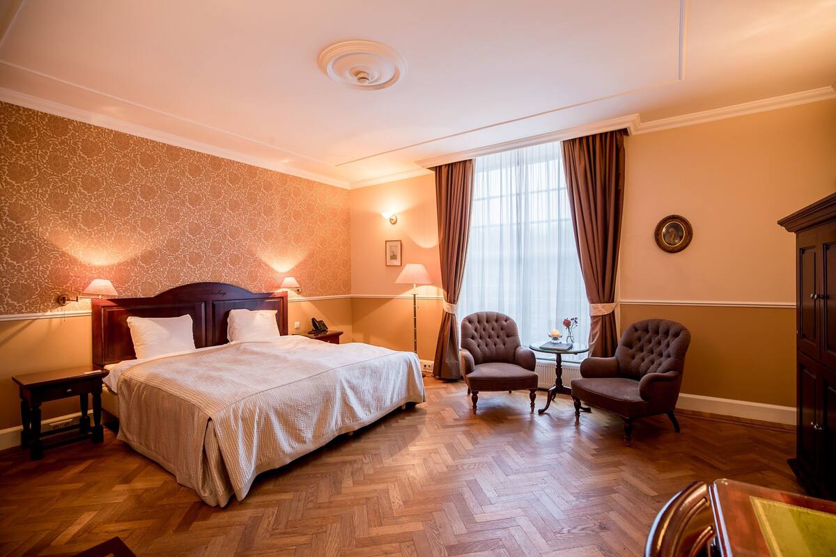 Une chambre d’hôtel comprenant un lit, deux fauteuils, une petite table et un meuble.