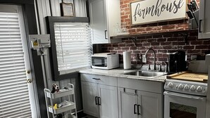 Een keuken met een boerderijbord, witte kasten, een magnetron, een koffiezetapparaat en een dubbele oven.