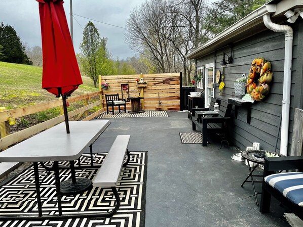 Un espace patio extérieur agrémenté d’une clôture en bois, d’un parasol rouge et d’une table recouverte d’un chemin de table à motifs.