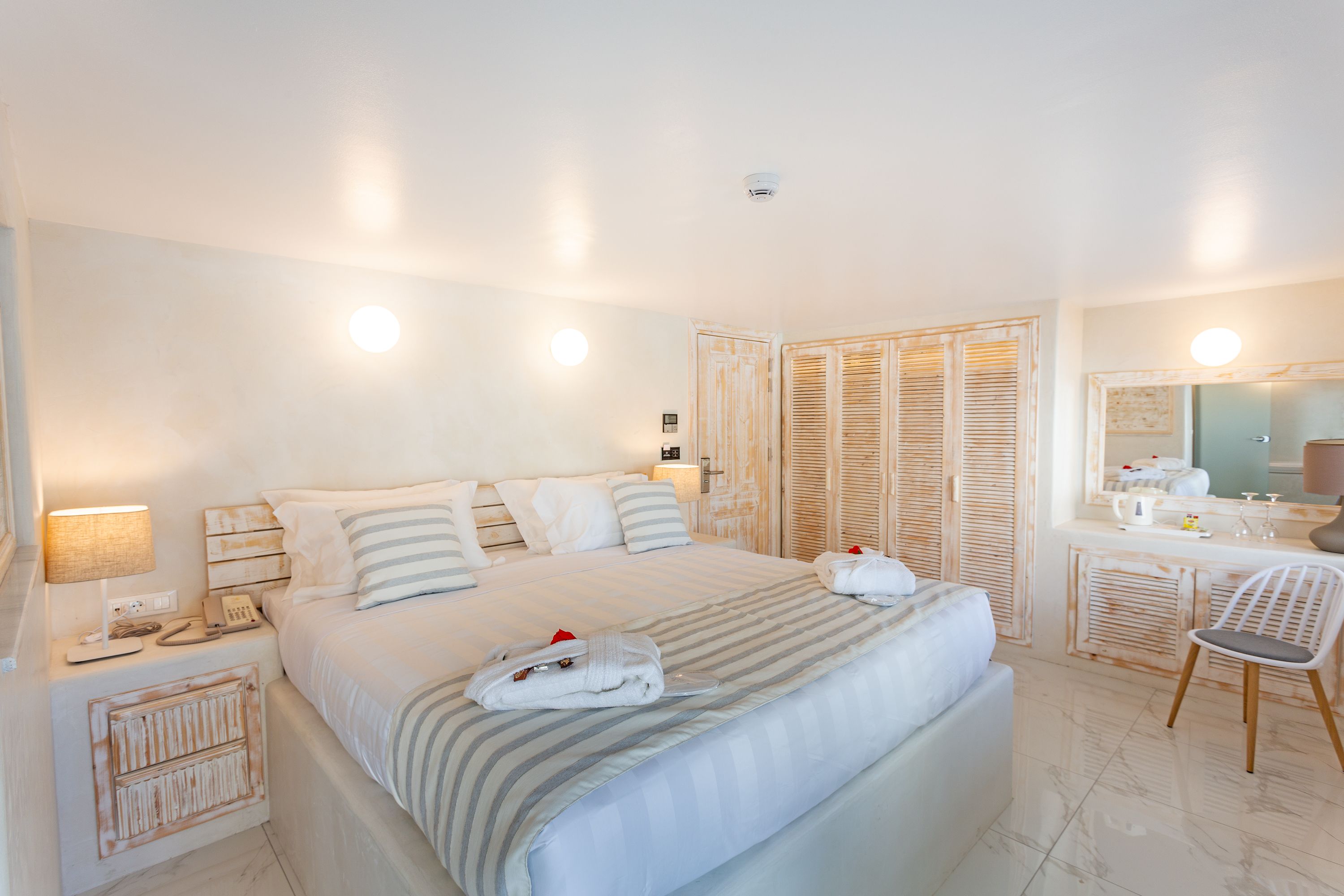 Una habitación de hotel con una cama grande, mesitas de noche, un escritorio con silla, un espejo y un armario.