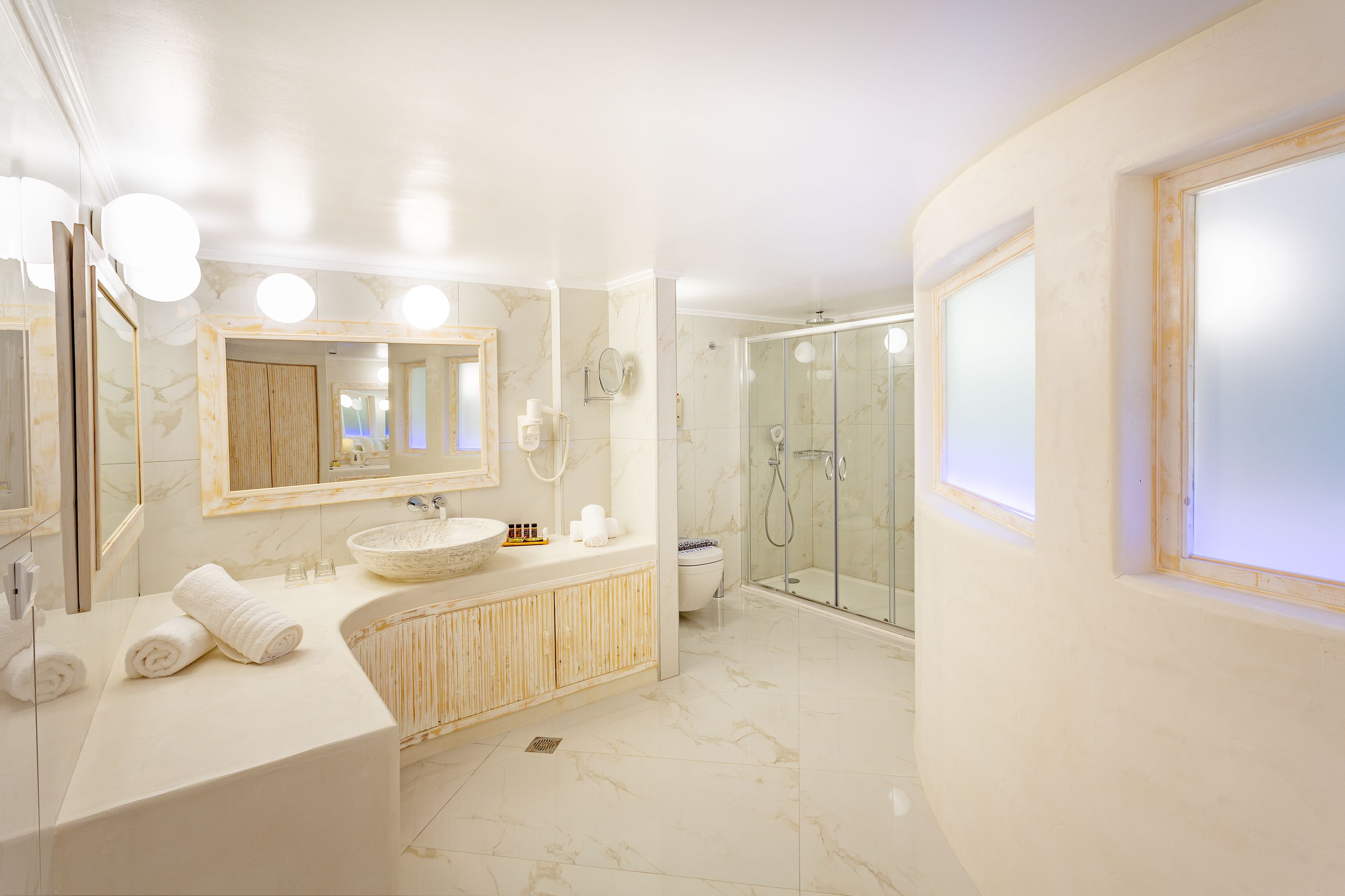 A modern bathroom with a large mirror, a round sink, a shower enclosure, and a toilet.