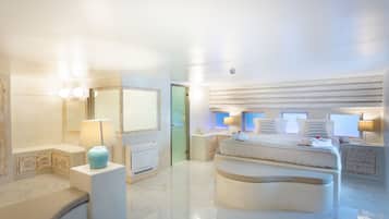 A spacious bedroom with a large bed, bedside tables, a vanity with a mirror, and a bathroom with a toilet and sink.