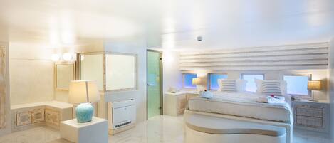 A spacious bedroom with a large bed, bedside tables, a vanity with a mirror, and a bathroom with a toilet and sink.