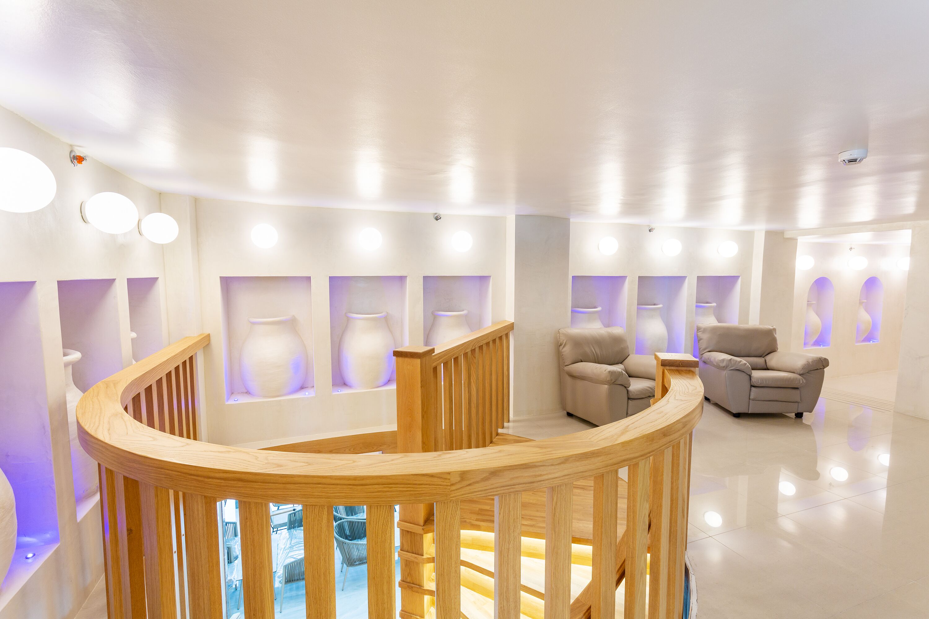 A modern interior with a wooden spiral staircase, seating area with sofas, and vases on shelves.