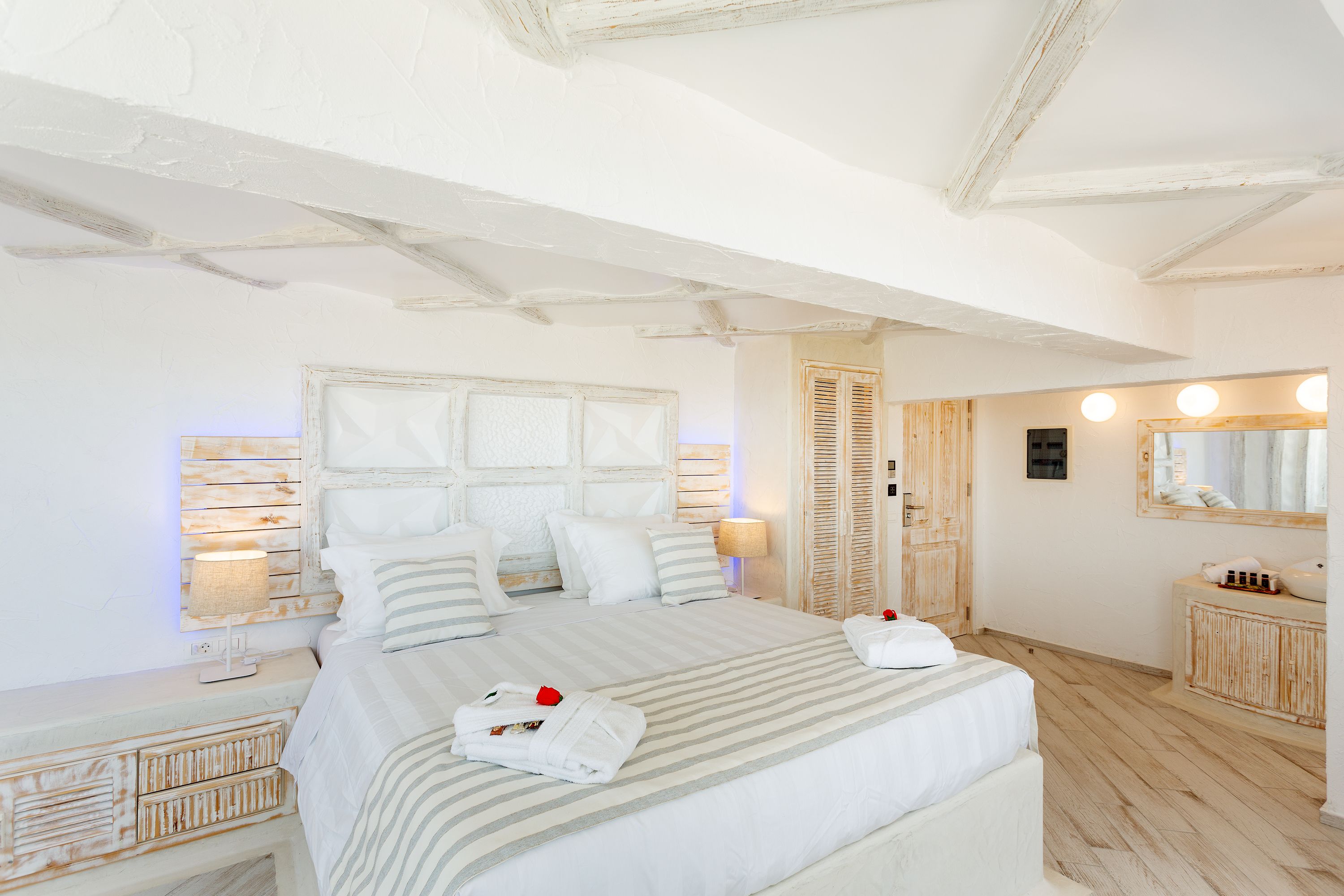 A neatly arranged bedroom with a large bed, bedside tables, a mirror, and a wooden wardrobe.
