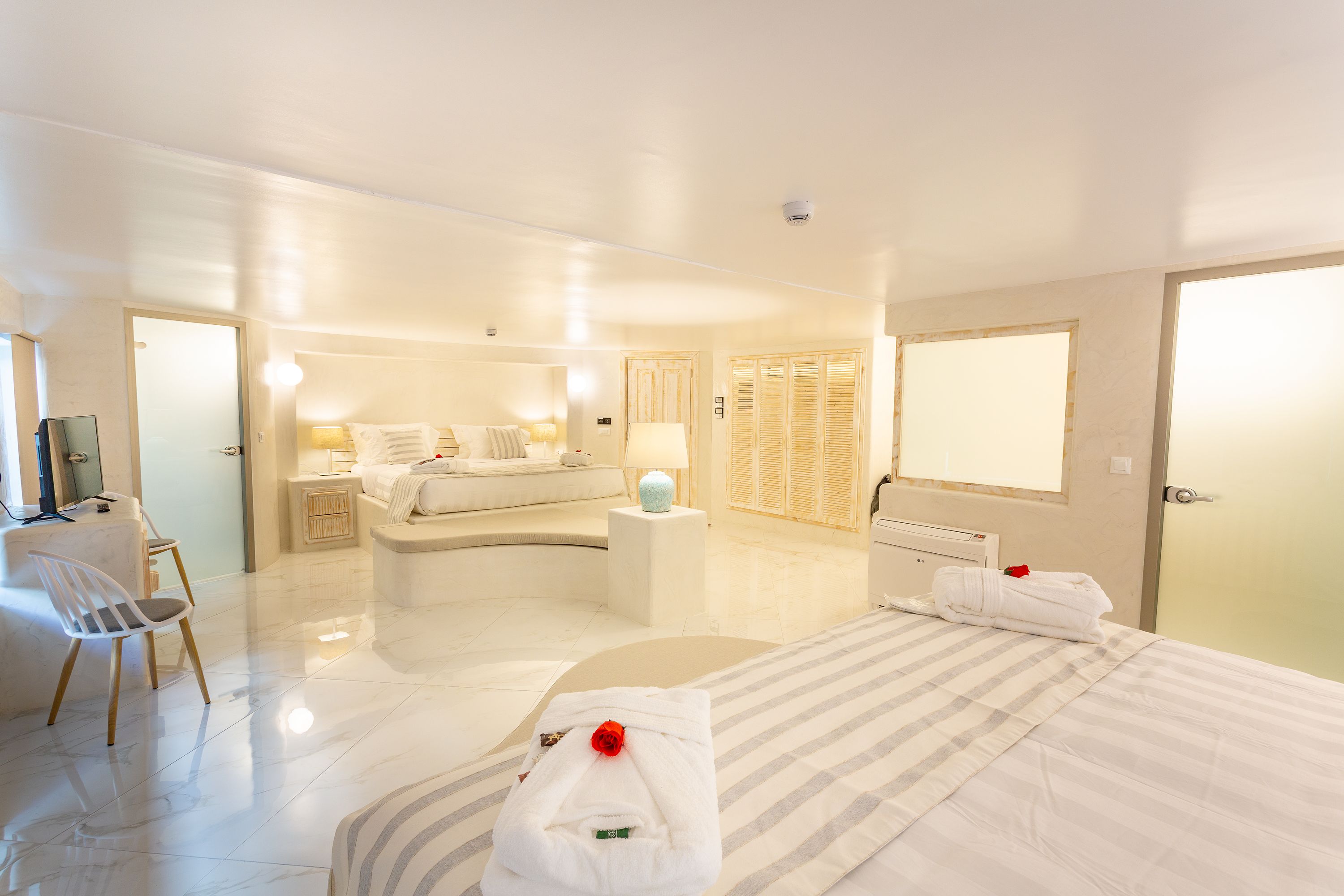 A hotel room with a bed, a desk, a chair, a window, and a door.
