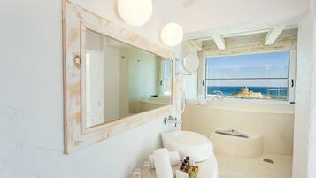 Een badkamer met een grote spiegel, een wastafel en een raam met uitzicht op zee.