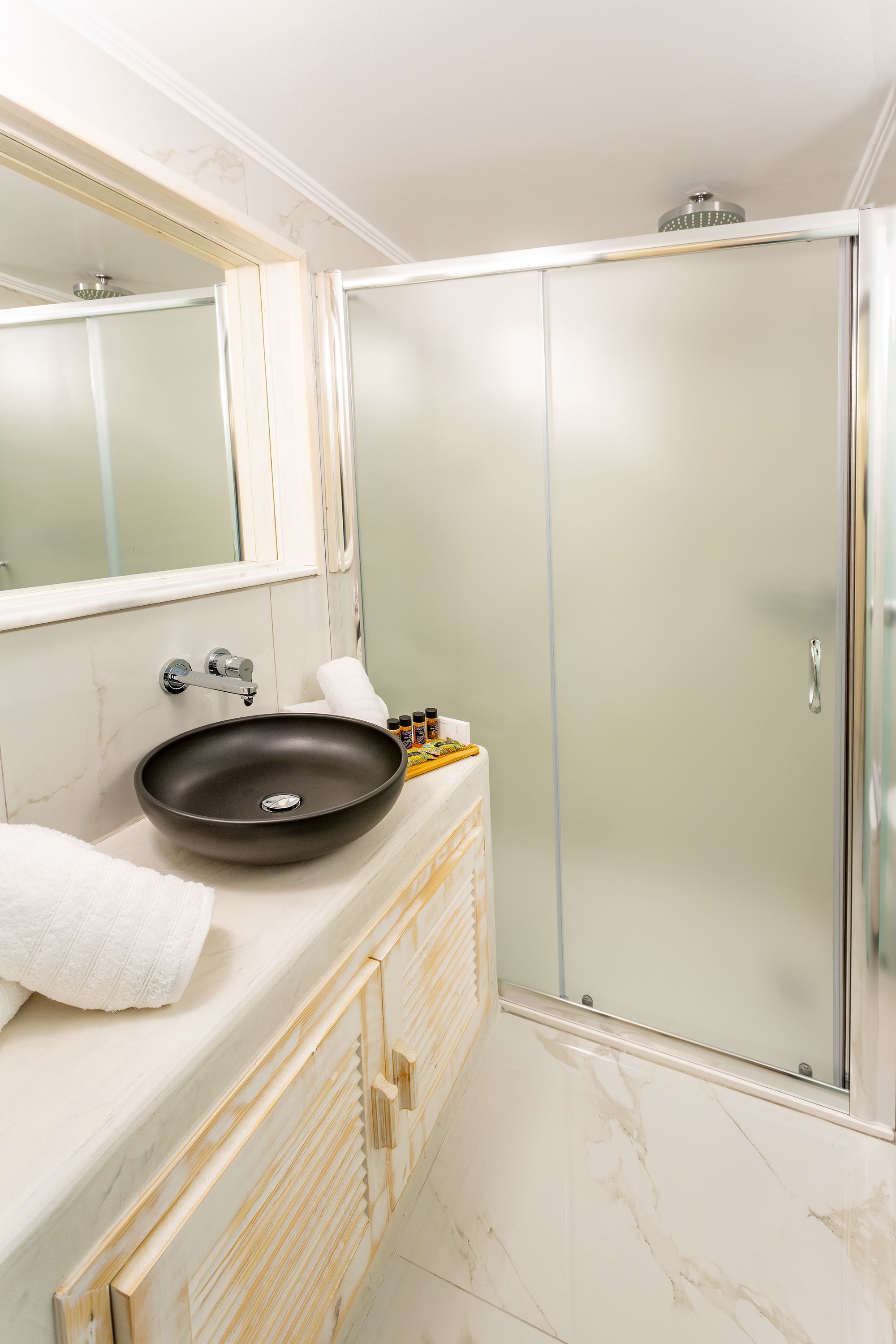 A bathroom with a large mirror, a round sink, a glass shower enclosure, and a wooden cabinet.