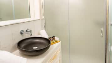 Een badkamer met een grote spiegel, een rond wastafelmeubel, een douchecabine van glas en een houten kast.