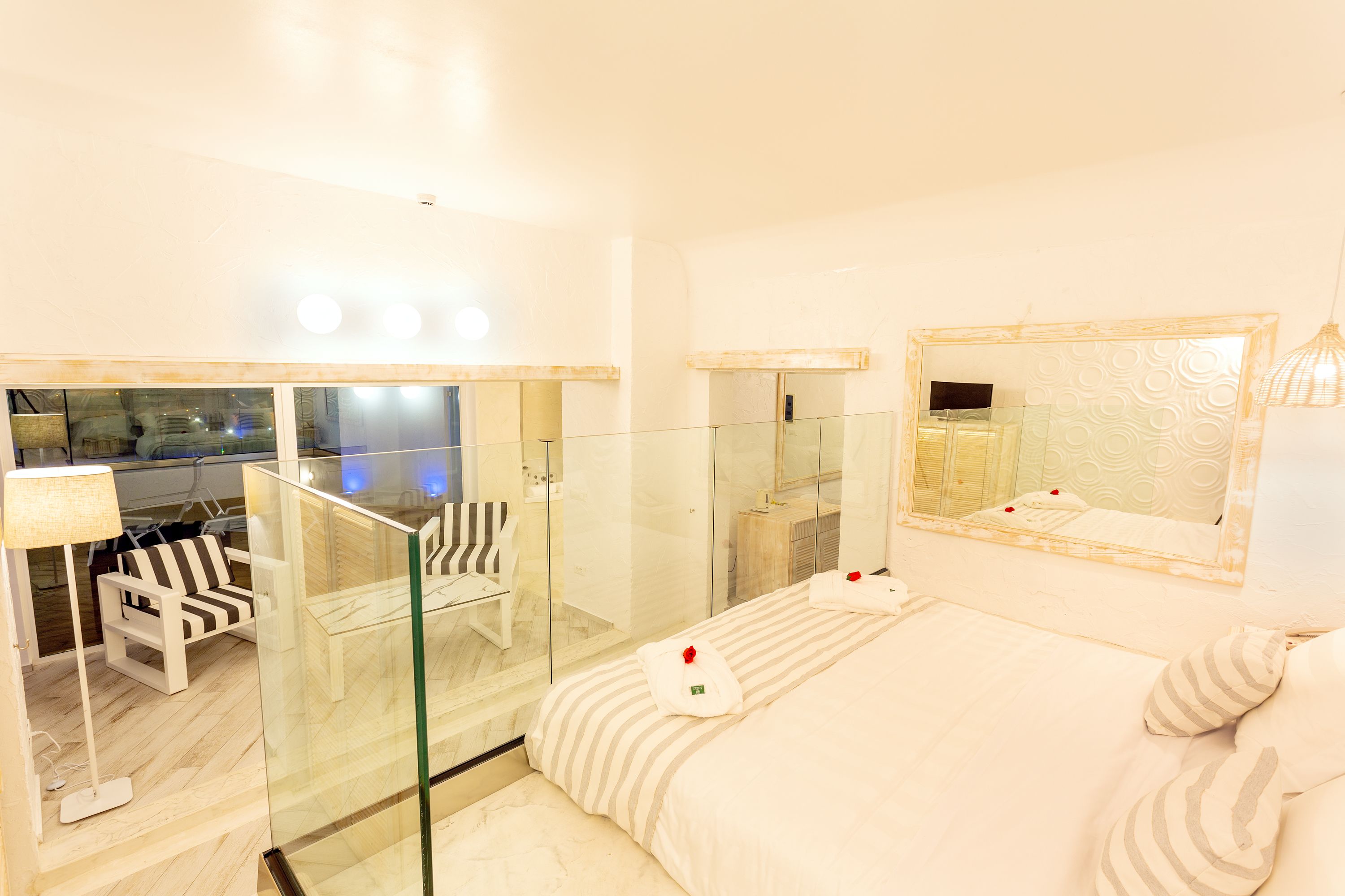 Ein Hotelzimmer mit einem Bett, einer in Glaswänden eingeschlossenen Dusche, einer Sitzecke mit einem Sessel und einem großen Spiegel.