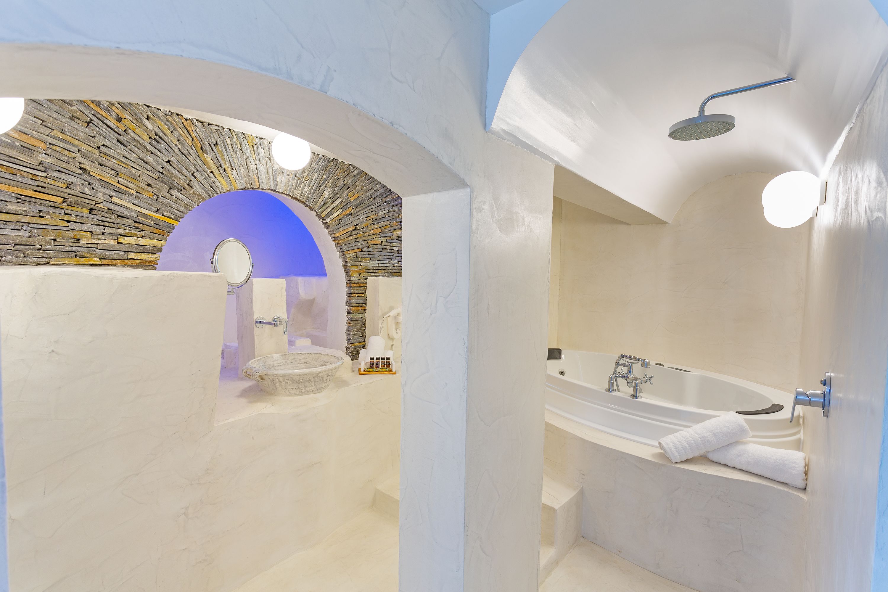 A modern bathroom with a stone arch, a bathtub, and a shower.