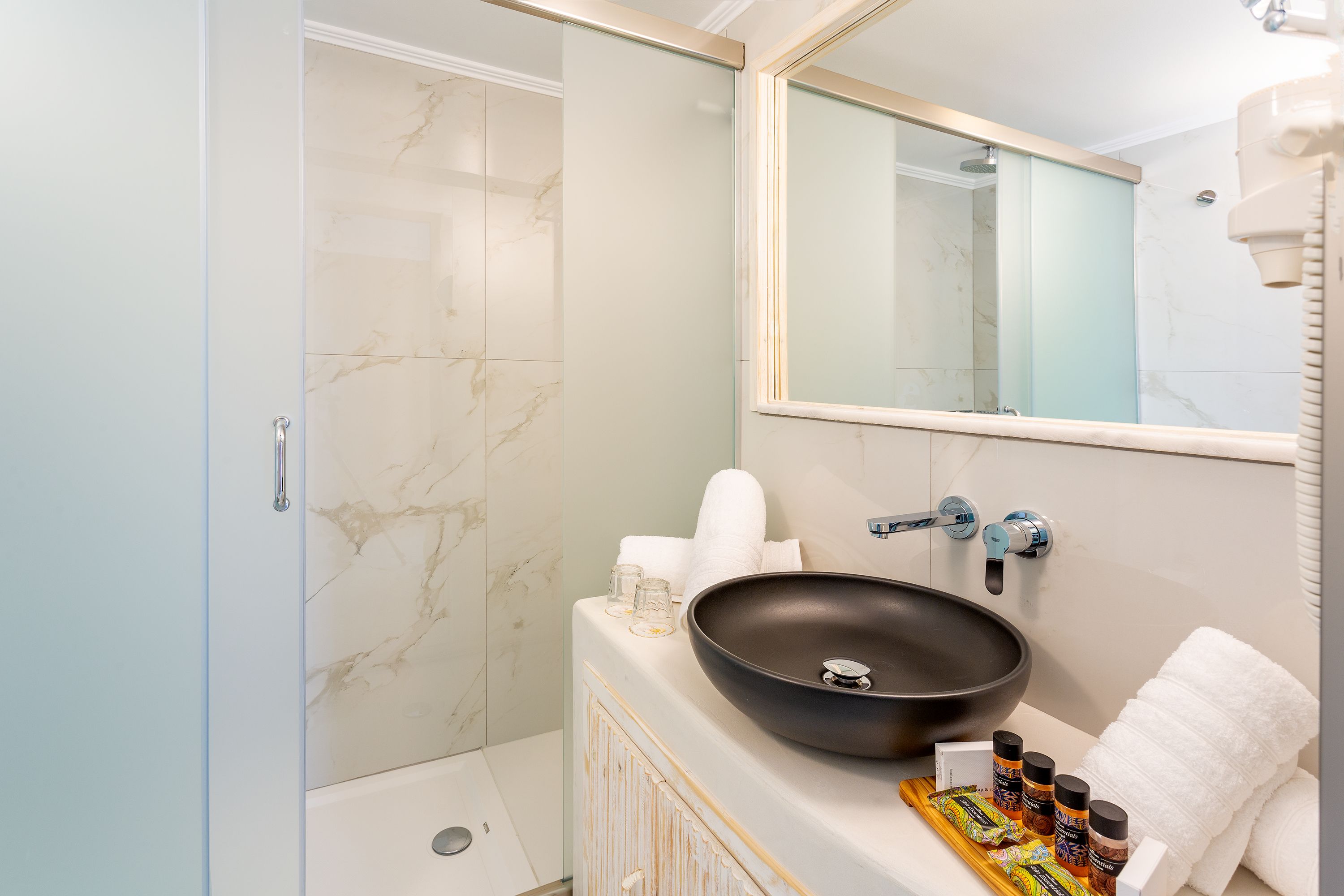 Un baño con un espejo grande, un lavabo tipo recipiente negro y una zona de ducha.