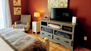 Una habitación de hotel con cama, una silla, un televisor y un aparador con cajones.