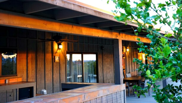Exterior de madera con un espacio de estar al aire libre cubierto, ventanas amplias y una puerta visible.