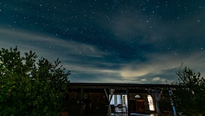 Un edificio rústico con un espacio exterior cubierto, un banco de madera y vista al cielo nocturno estrellado.