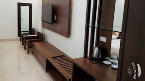 Um saguão de hotel com um longo banco de madeira, uma televisão de tela plana na parede e um espelho refletindo parte do espaço.