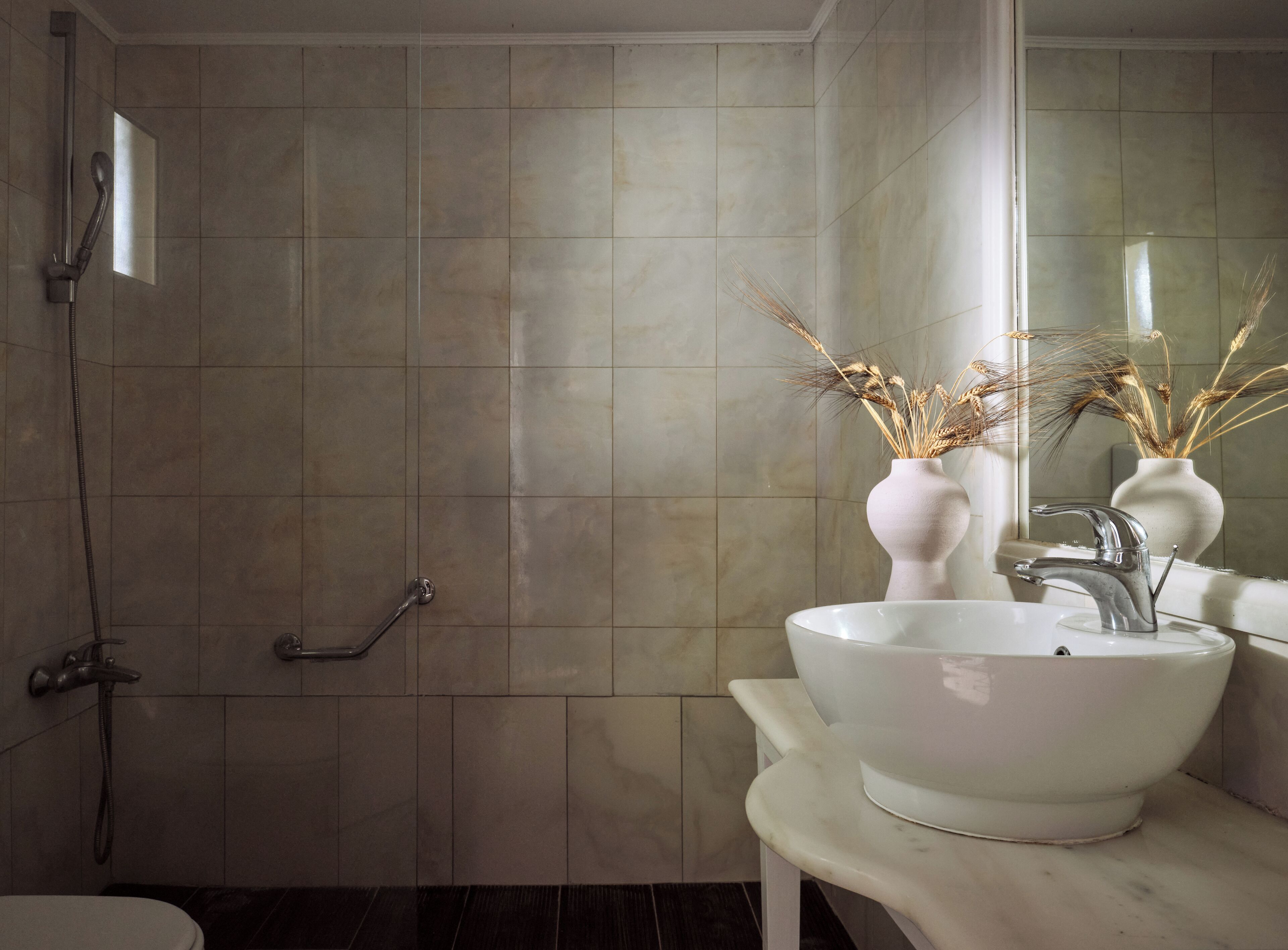 A bathroom with a shower, a sink with a vase of dried plants, and a mirror.