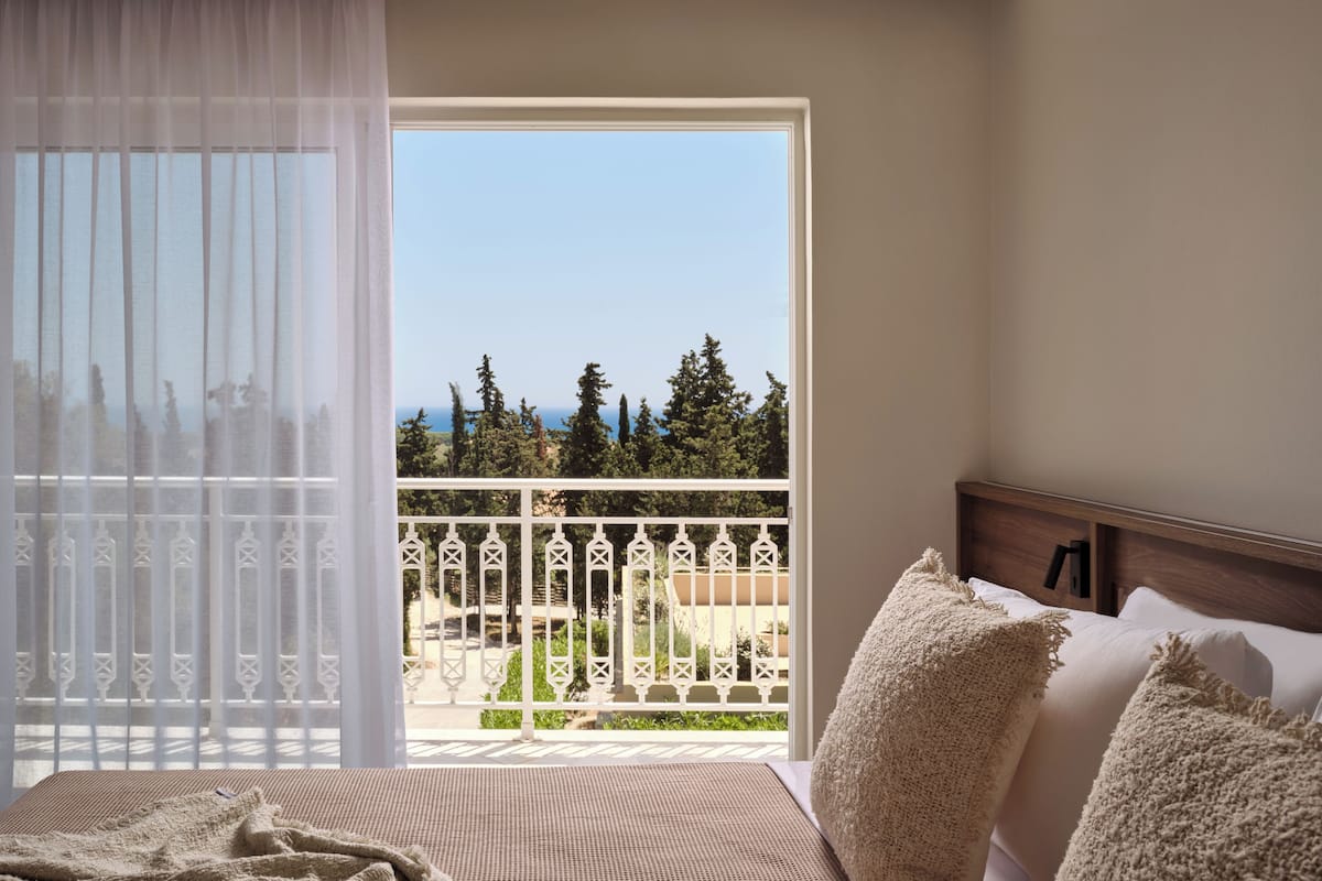 Un dormitorio con balcón, cama y vistas a árboles y al mar.