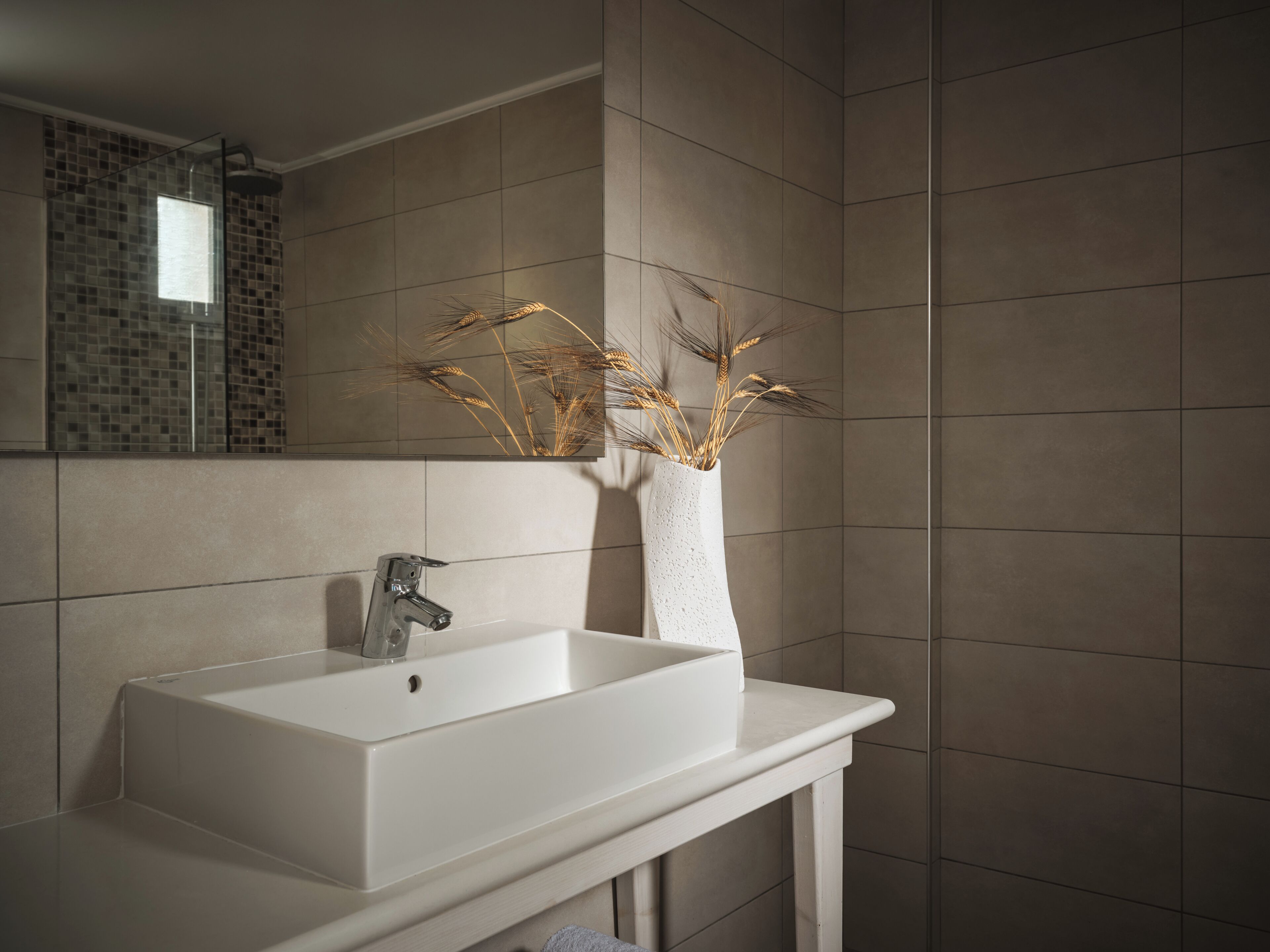 A bathroom with a white sink, a mirror, and a vase with dried wheat stalks.