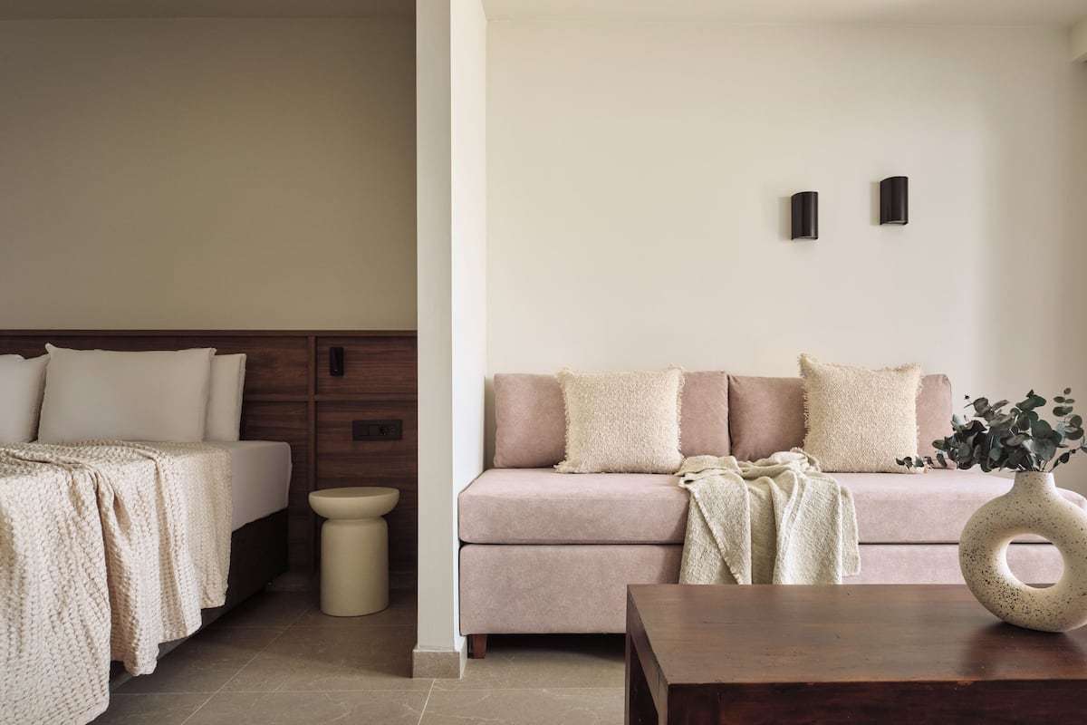 Un dormitorio con cama, mesita de noche, pequeño taburete junto a la cama, sofá y lámpara de pared.