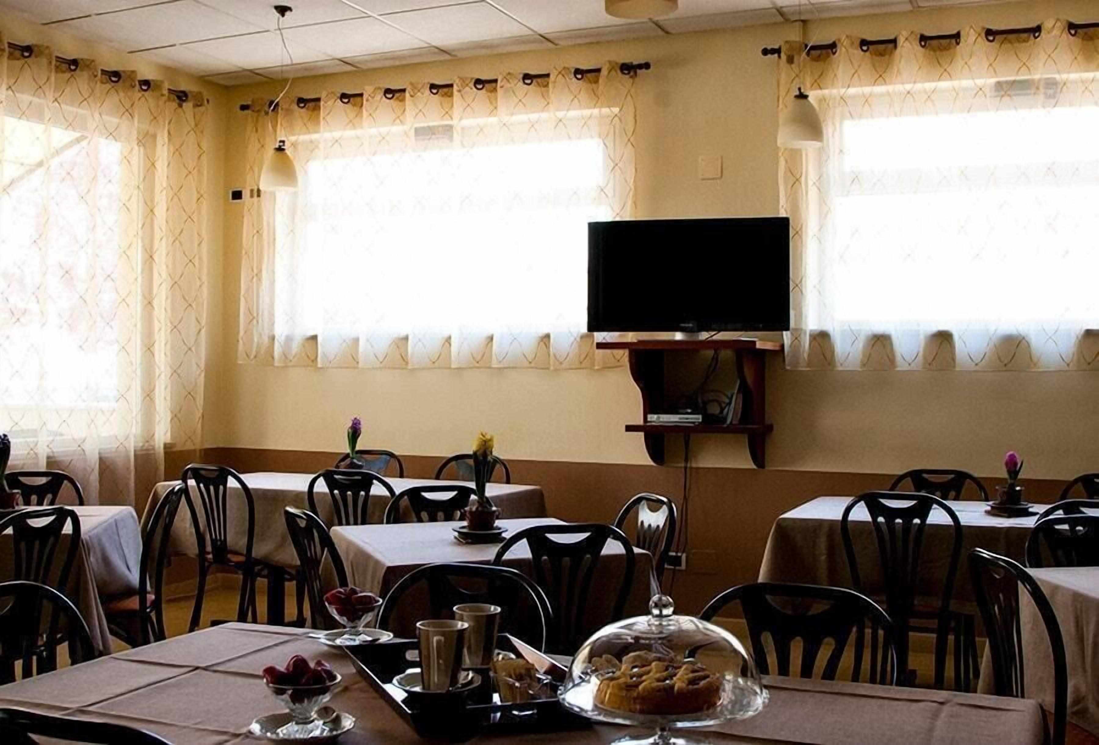 Un espace repas avec des tables et des chaises, un téléviseur fixé au mur et des fenêtres avec des rideaux.
