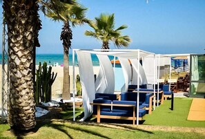 A beachside lounge area with white canopies, blue lounge chairs, and a view of the ocean. - Hotel La Pergola (Alba Adriatica)