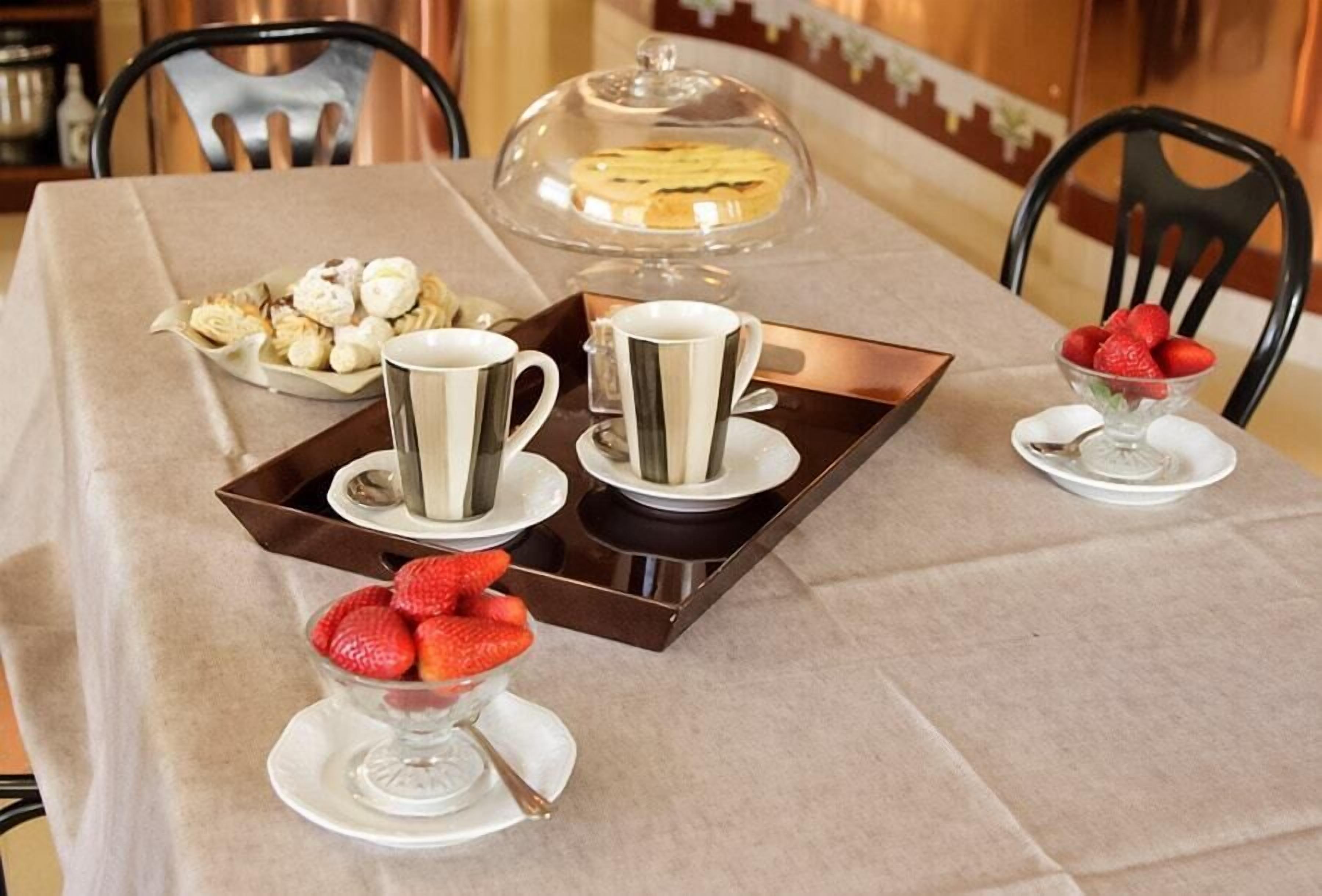 A table set with a tray of pastries, two cups, a bowl of strawberries, and a covered dessert.