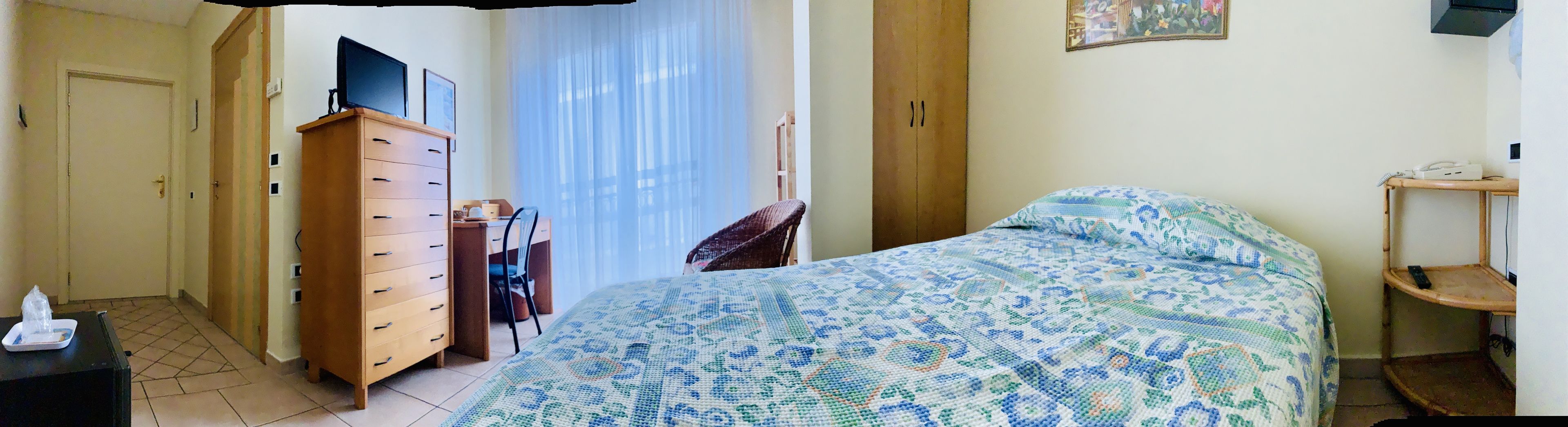 Une chambre à coucher avec un lit, une commode en bois, une chaise, un bureau et une fenêtre avec des rideaux.