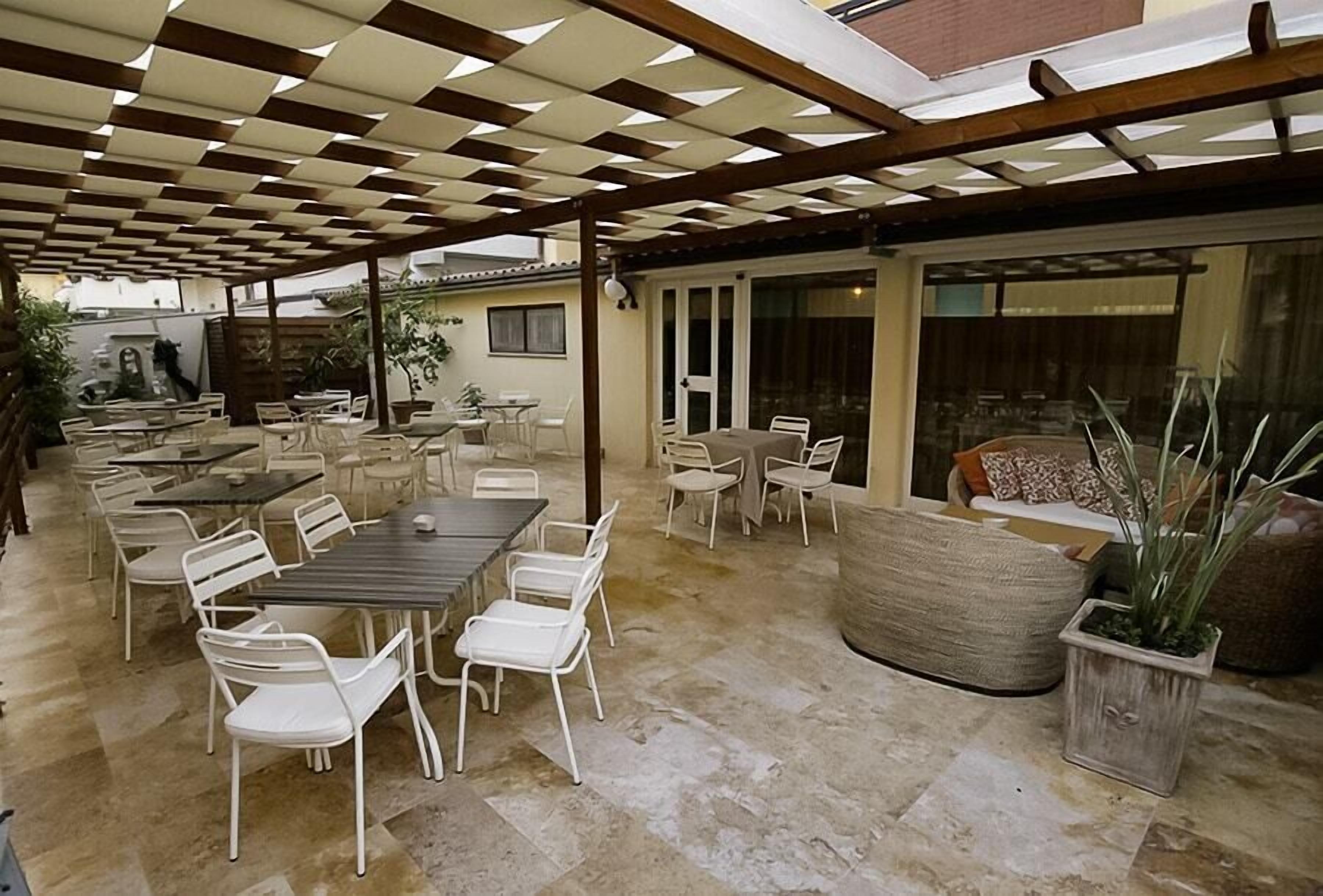 Un patio al aire libre con varias mesas y sillas, una maceta grande de fibra natural y una pérgola.