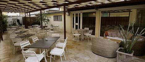 Un patio al aire libre con varias mesas y sillas, una maceta grande de fibra natural y una pérgola.