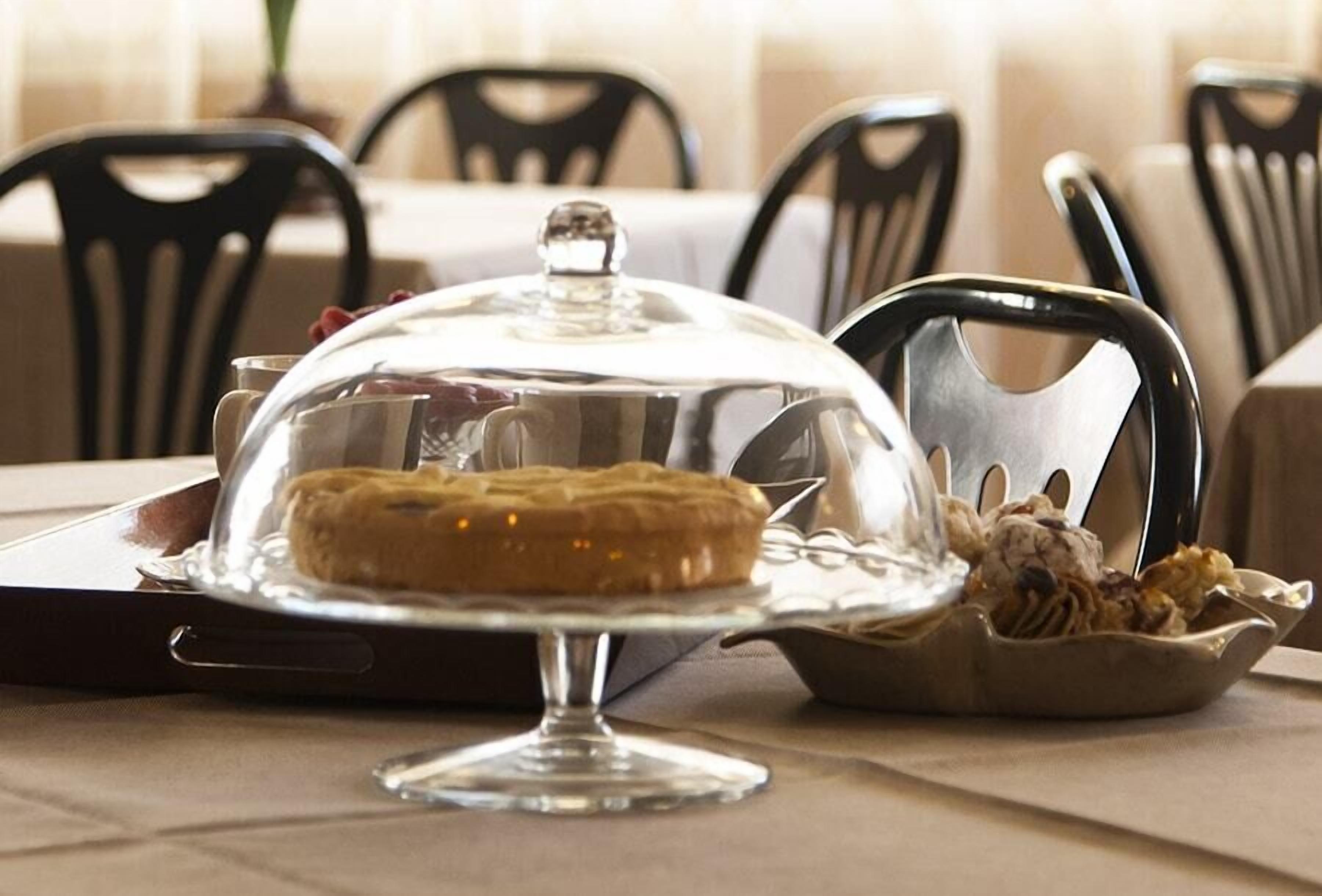 A dessert on a glass stand with a clear dome cover, accompanied by a bowl of what appears to be a salad or side dish.