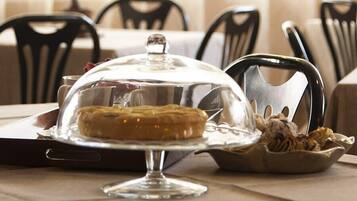 A dessert on a glass stand with a clear dome cover, accompanied by a bowl of what appears to be a salad or side dish.