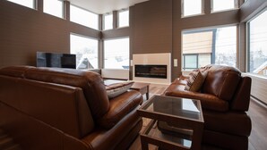 A spacious living room with leather sofas, a glass coffee table, and a fireplace. - Mountain Butterfly (Kutchan)