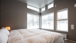 A bedroom with a large bed, multiple windows, and a radiator. - Mountain Butterfly (Kutchan)