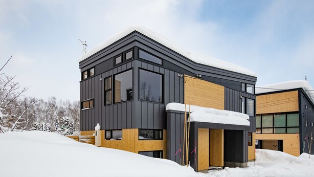 A modern two-story building with a dark exterior and wooden accents, surrounded by snow. - Mountain Butterfly (Kutchan)
