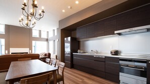 A modern kitchen with dark cabinetry, a built-in oven, and a dining area with a wooden table and chairs. - Mountain Butterfly (Kutchan)