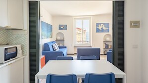 A modern living room with a white table and blue chairs, a blue sofa, and a view of the city through a large window. - JOIVY La Finestra Sulla Piazzetta a Portofino (Portofino)