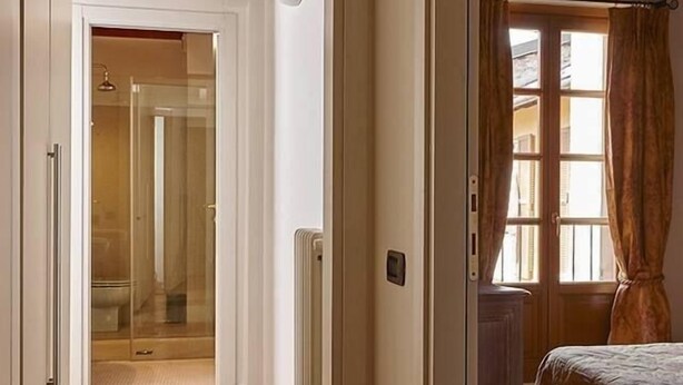 Un pasillo con suelo de madera que conduce a un dormitorio con cama y ventana con cortinas.