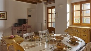 Un comedor con una mesa de madera dispuesta para una comida, un televisor sobre un escritorio y una ventana con vistas.