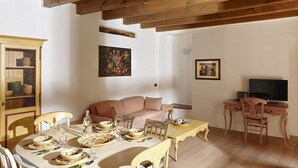 Un comedor con una mesa de madera dispuesta para una comida, un sofá y un televisor al fondo.
