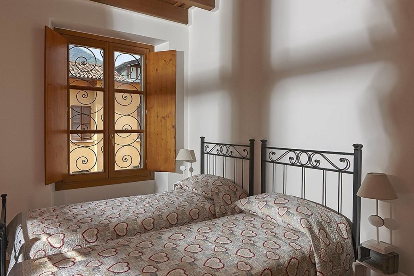 Ein Schlafzimmer mit einem Bett, einem Fenster mit geöffneten Fensterläden und einem Nachttisch mit einer Lampe.