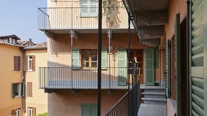 Un edificio de varios pisos con balcones, contraventanas verdes y una escalera que conduce a la entrada.